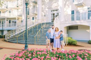 A group poses near pink flowers outside Disney's Beach Club Resort with its distinctive blue and white architecture.