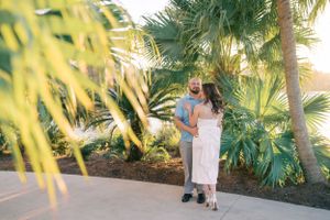 A couple shares a romantic moment on a pathway surrounded by lush tropical palm trees at sunset.