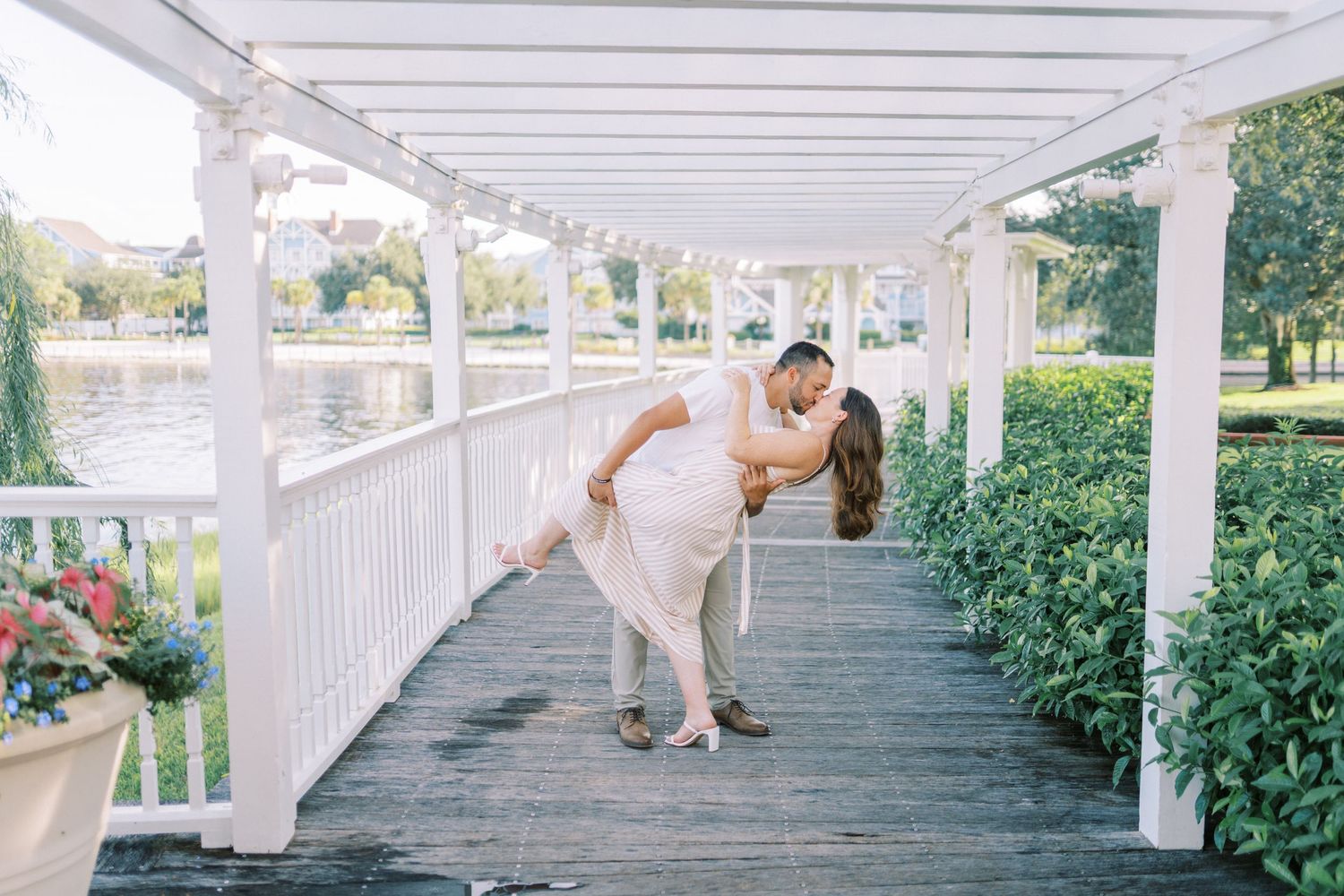 A couple shares an intimate dance moment under a white pergola surrounded by lush greenery and natural light.