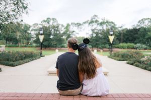 Two people sit together on a bench overlooking a scenic park pathway on a sunny afternoon.