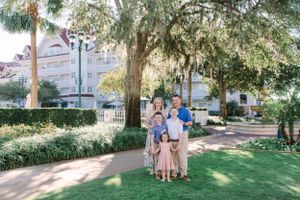 A family enjoys a sunny afternoon on a lush green lawn with Spanish moss draped trees and resort buildings in the background.