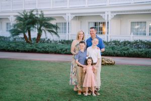 A family group poses together on manicured resort grounds with a white colonial-style building facade behind them.