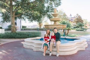 Three people sit together on an ornate stone fountain in a landscaped garden setting during daytime.