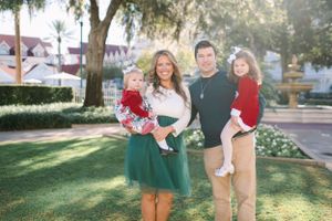 A family stands together on a sunny lawn with green hedges and architecture in the background.