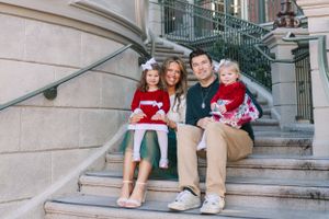 Group wearing holiday sweaters sits together on outdoor stone steps of a building in warm light.