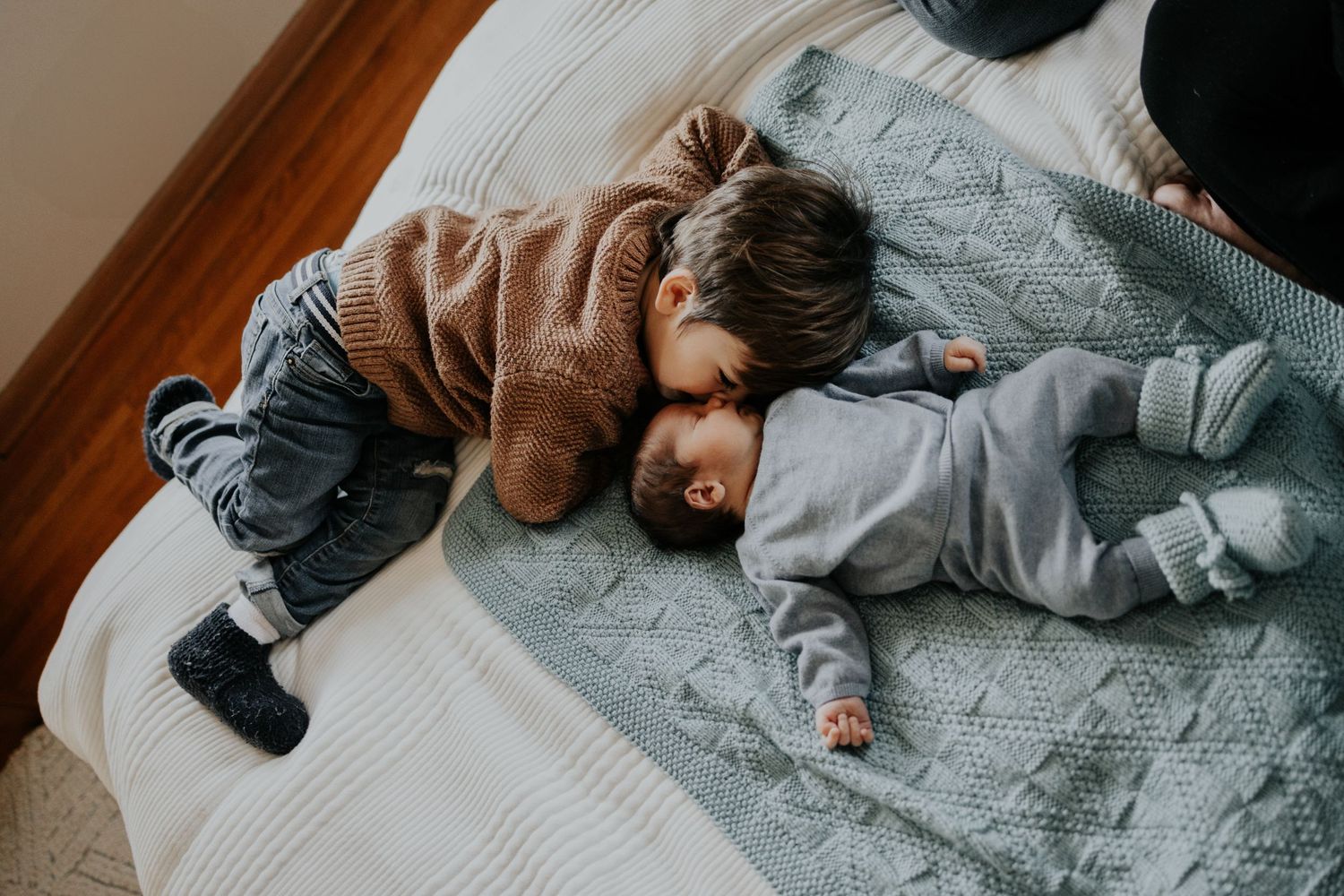 Two small children nap together on a cozy gray blanket while wearing sweaters and pants.