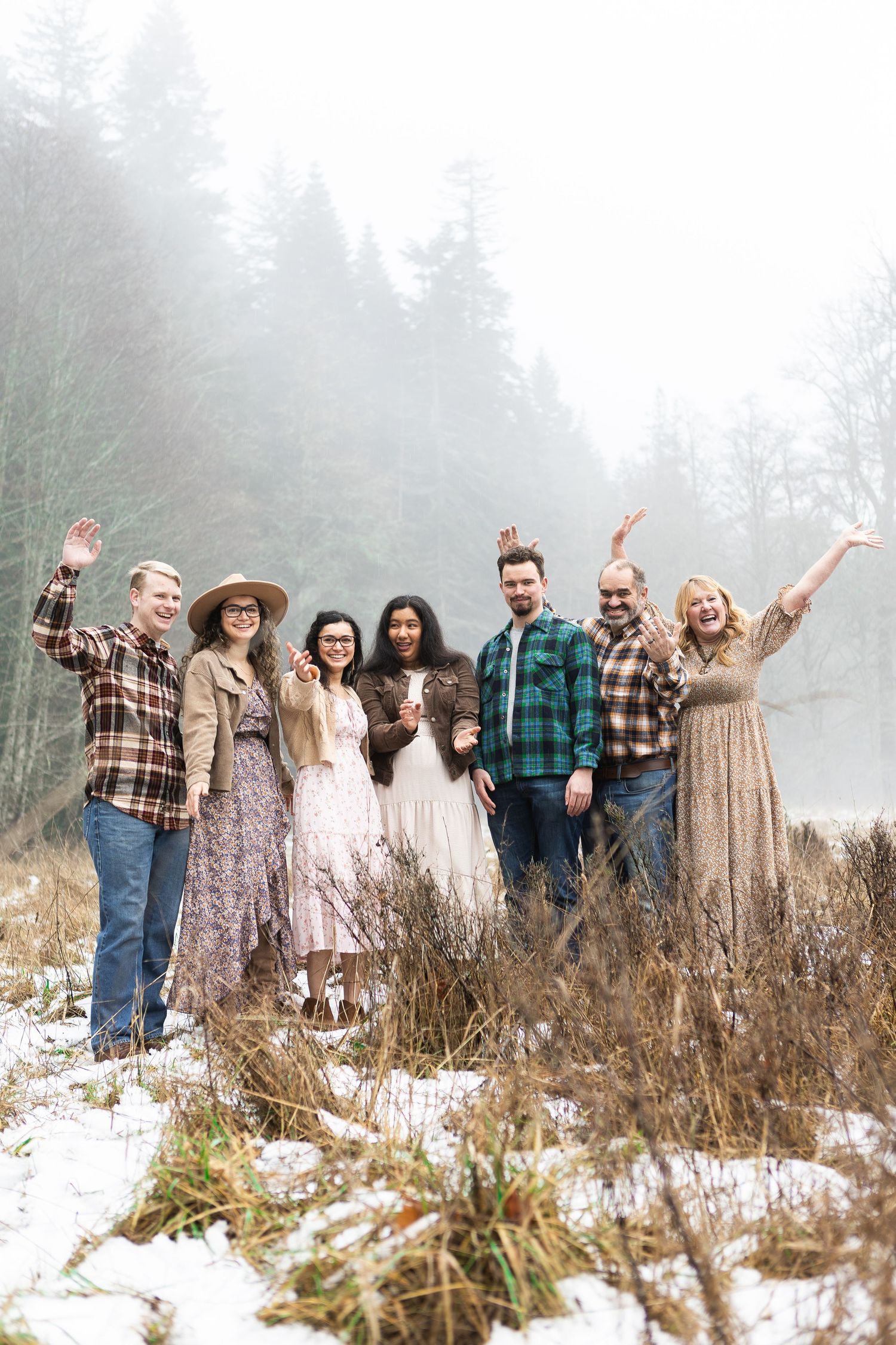 Group of people celebrating outdoors in winter with fog and snow, wearing flannels and dresses in rustic setting.