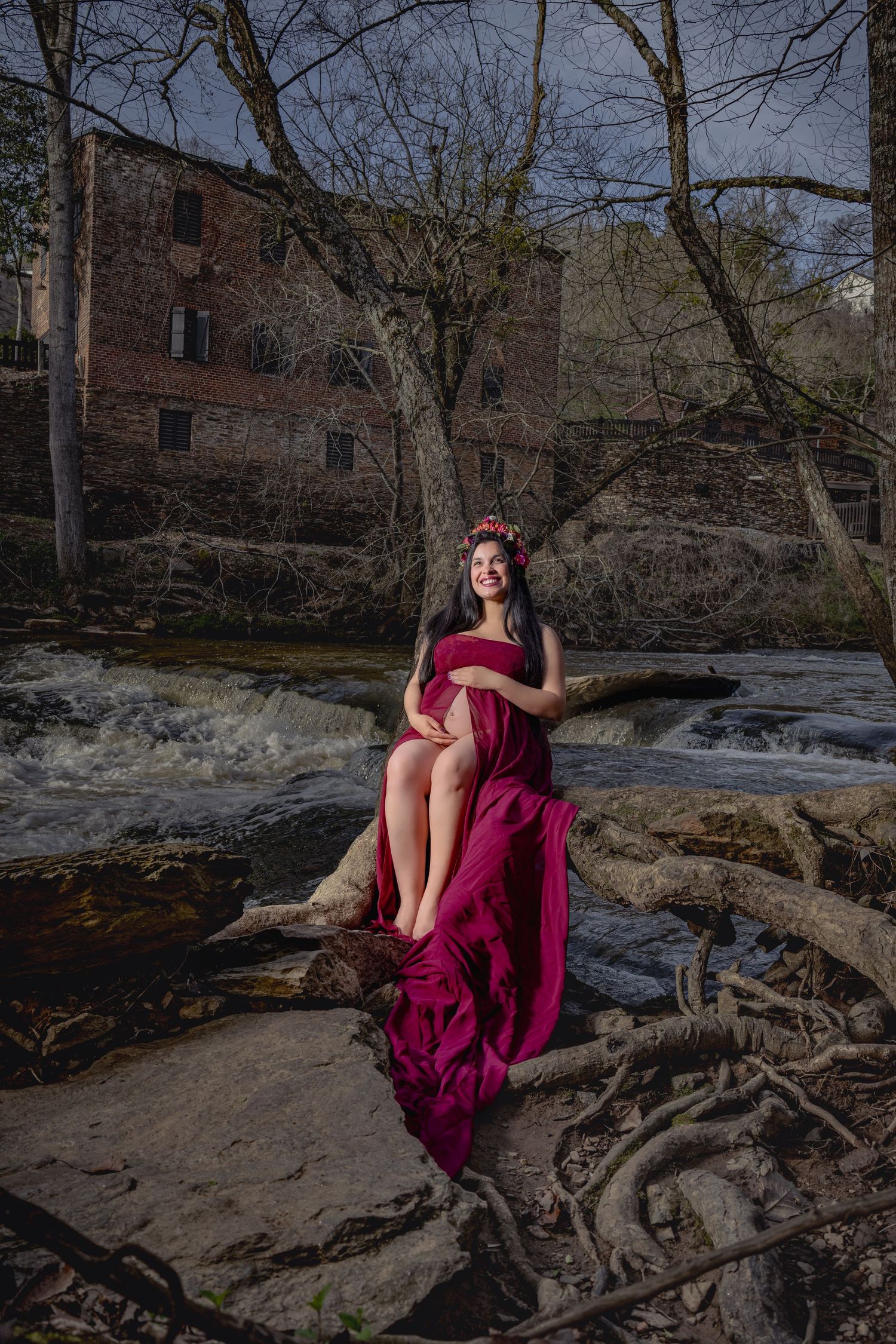 A dramatic photoshoot on fallen tree branches features a flowing burgundy dress against a winter landscape.