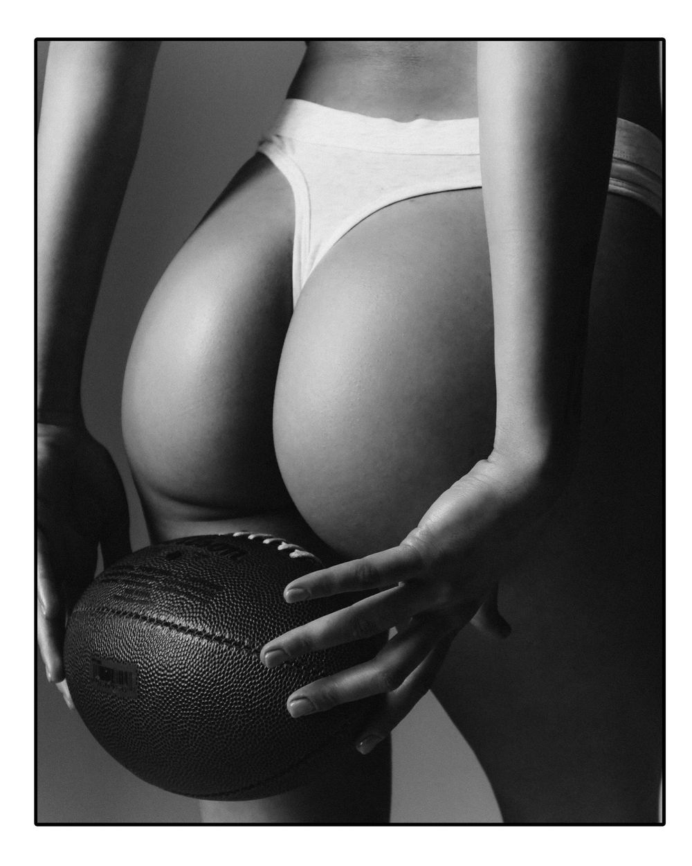 A black and white artistic sequence showing a football being held against a bare torso in dramatic lighting.