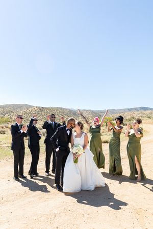 Wedding party celebrates outdoors in desert landscape with mountains in background on sunny day.