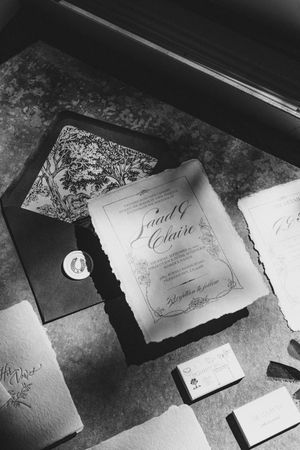 Elegant calligraphy wedding invitations and name cards with deckled edges arranged in black and white lighting.