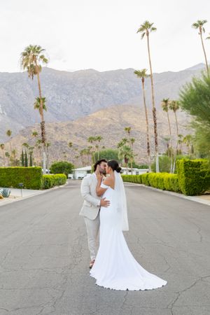 Newlyweds embracing on a palm tree-lined street with mountain backdrop in Palm Springs.