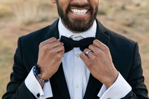 Close-up view of hands adjusting a black bow tie on a formal tuxedo with white dress shirt and cufflinks.