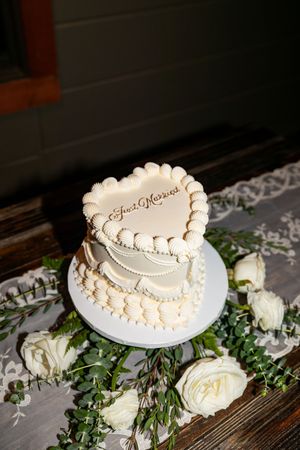 Elegant white heart-shaped wedding cake decorated with delicate pearls and floral accents on a rustic wooden table.