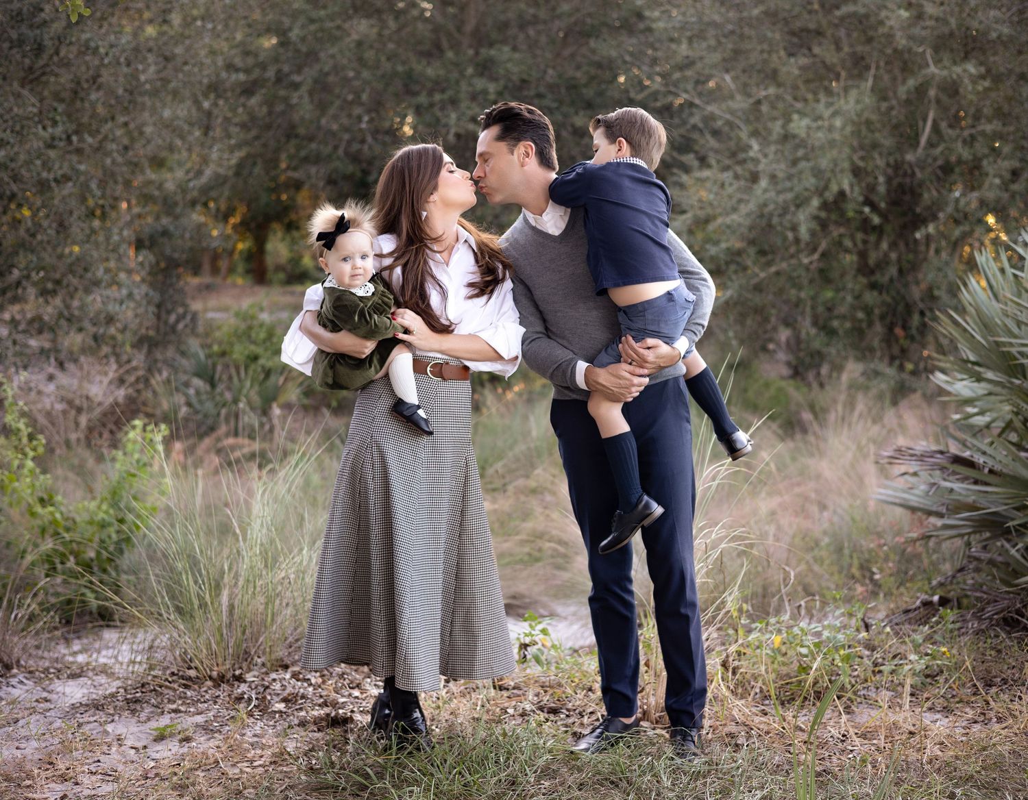 A family shares tender moments while holding their two minor children in a south Florida park with natural scenery.