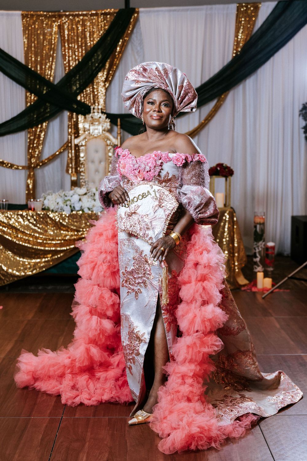 Elegant celebration scene with pink ruffled tulle train and sparkly sequined dress against gold and black draped backdrop.