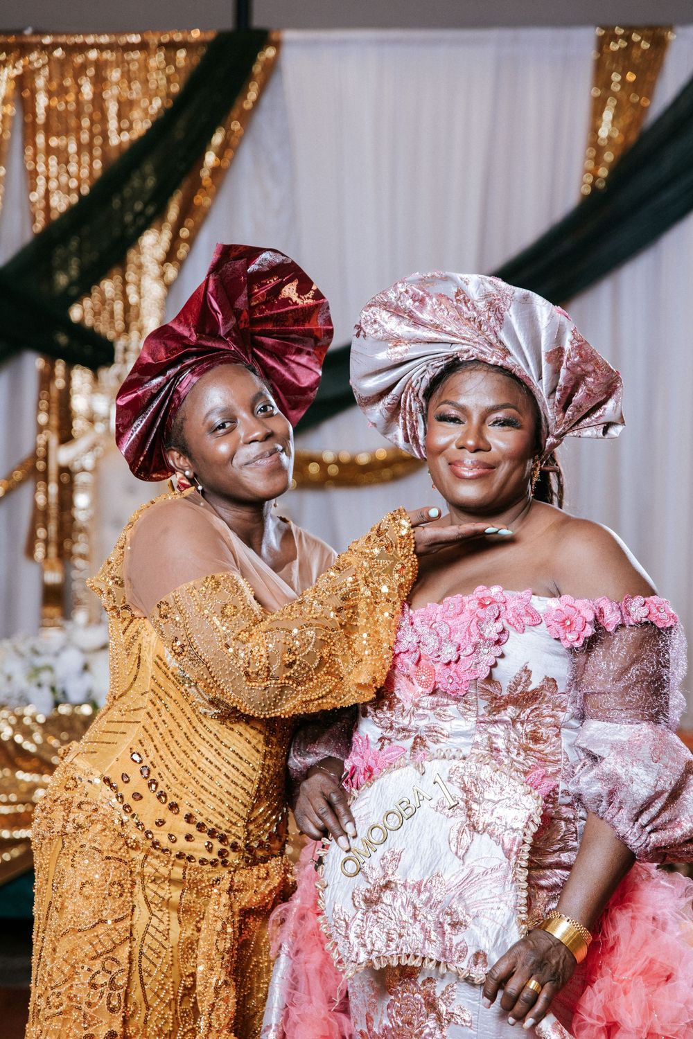 Traditional celebration featuring elegant gold and pink attire with ornate headpieces in luxurious setting.