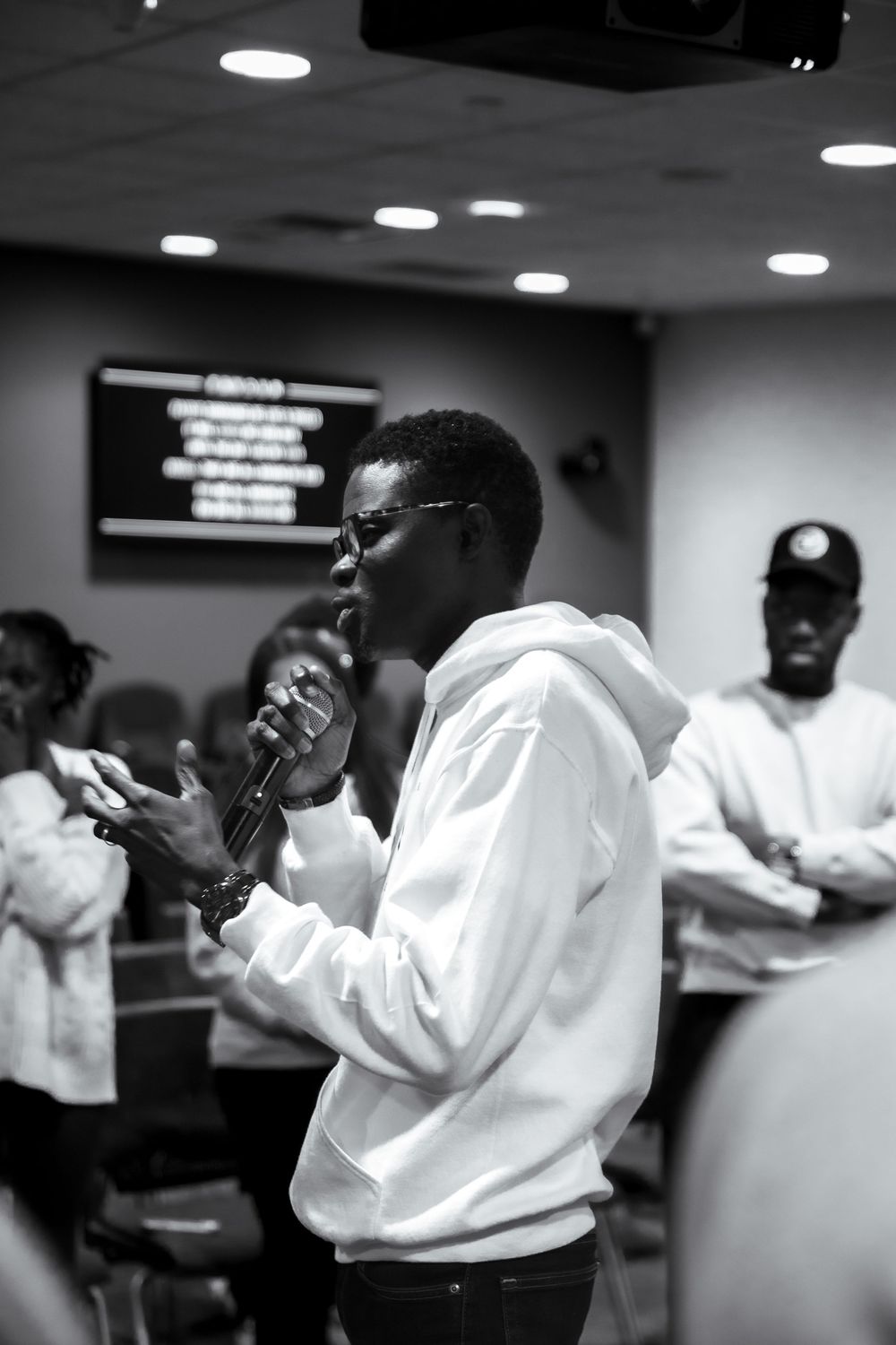 A person in a white shirt gestures dramatically while performing in a dimly lit indoor space.