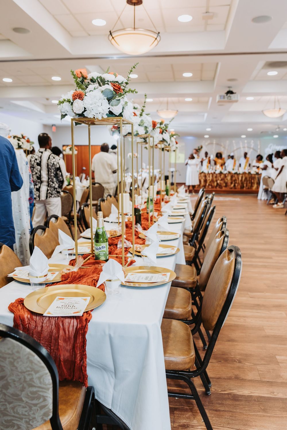 Elegant wedding reception tables decorated with white linens, coral accents, and floral centerpieces in a spacious ballroom.