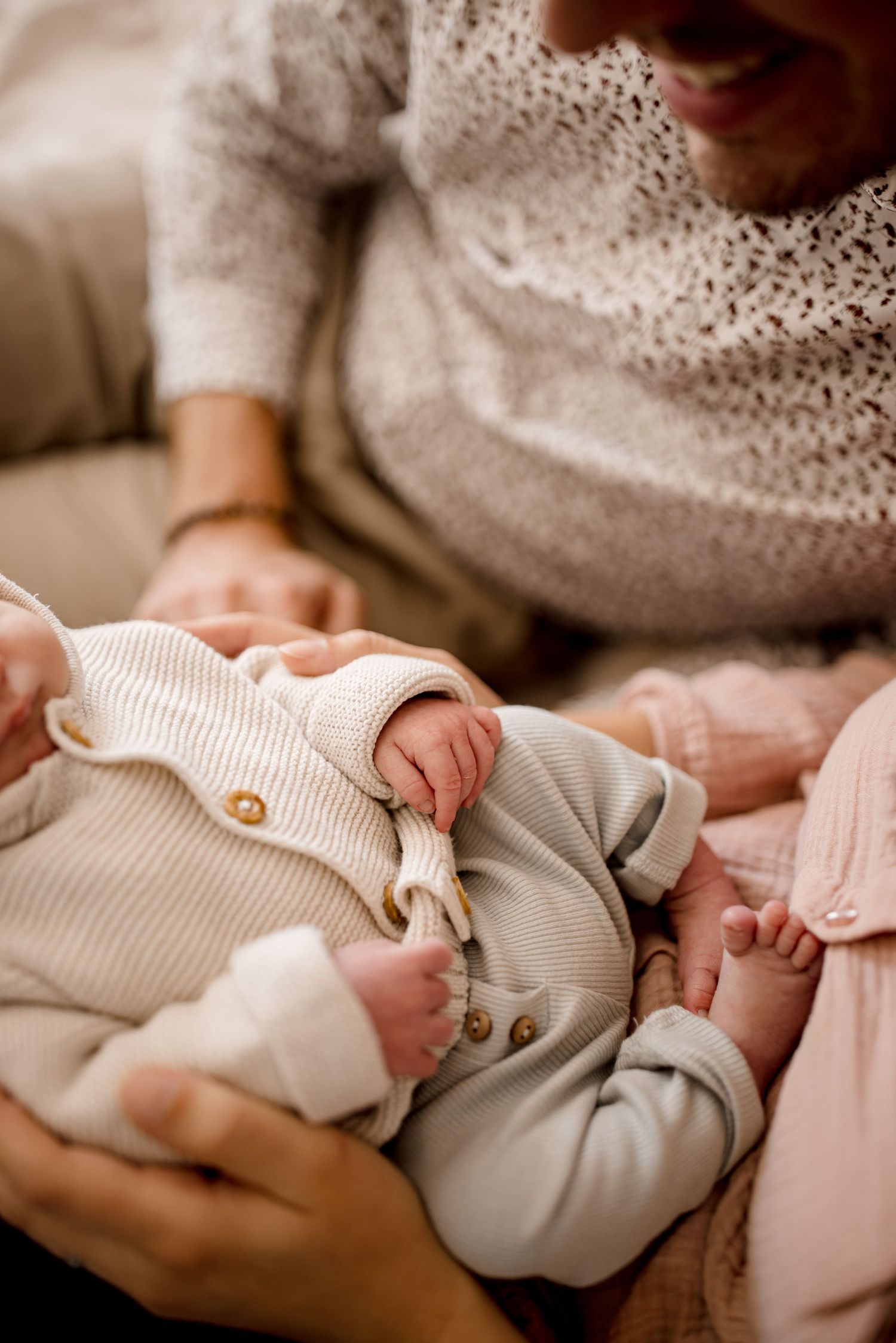 Gros plan d'un bébé portant une tenue en tricot blanc avec des détails de boutons pendant qu'il est bercé.