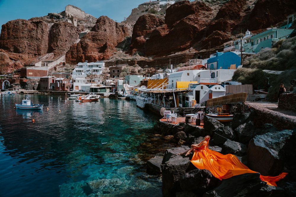 Coastal village with fishing boats and vibrant orange fabric flowing over harbor rocks.