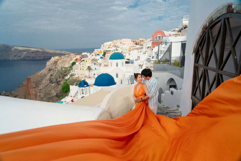 Flowing orange dress fabric creates dramatic scene against classic Santorini architecture.