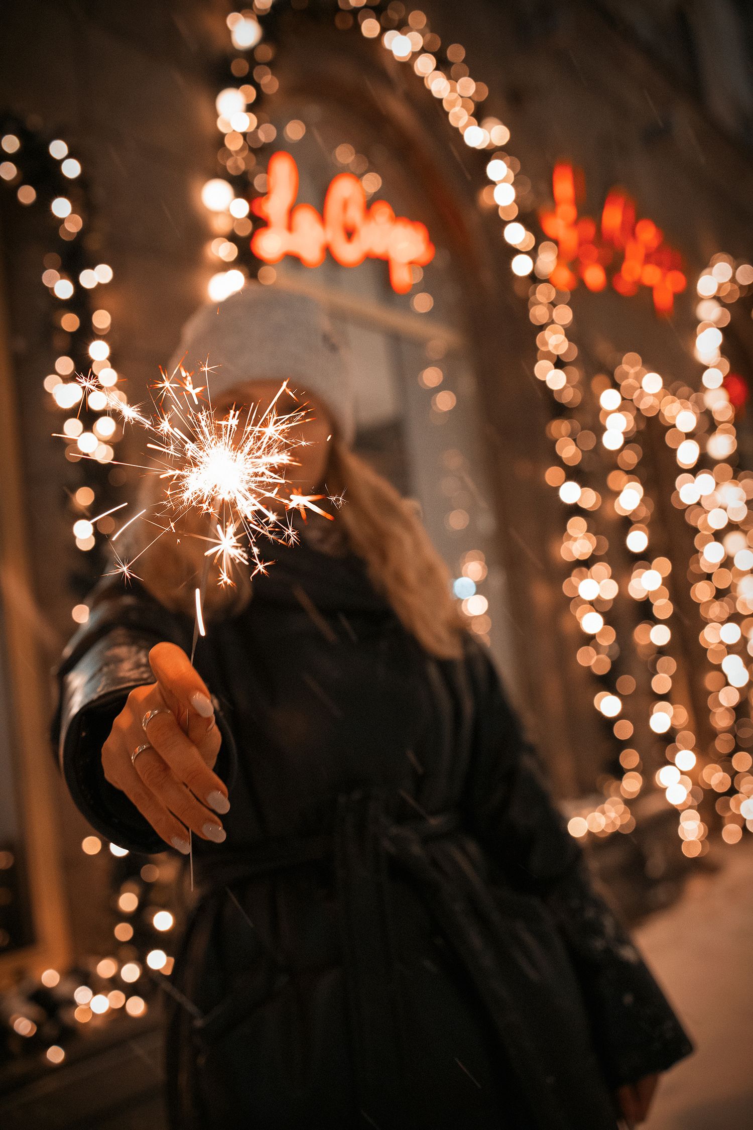 girl holding sparkler close to camera. in the background - bokeh from street lighting.