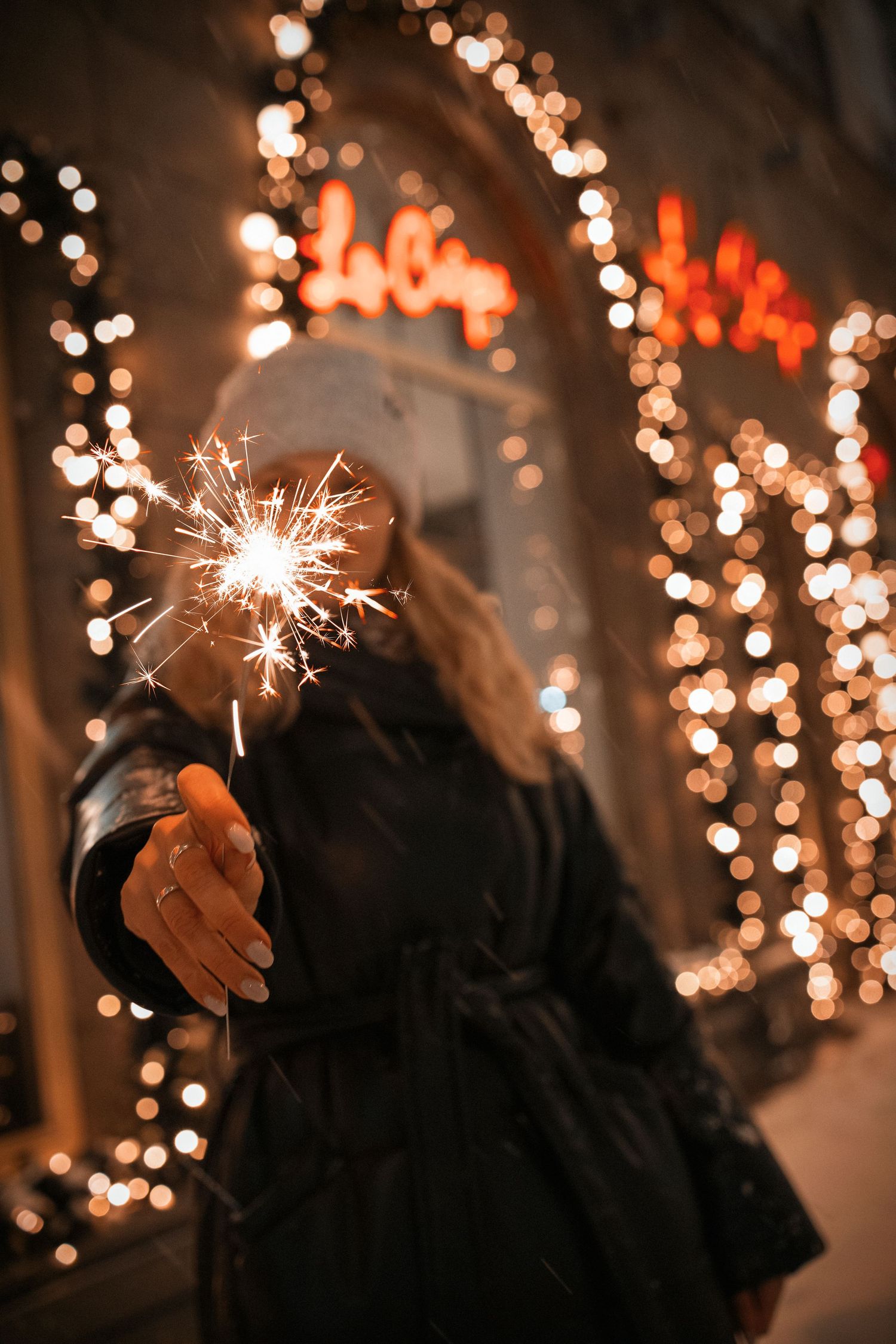 girl holding sparkler close to camera. in the background - bokeh from street lighting.