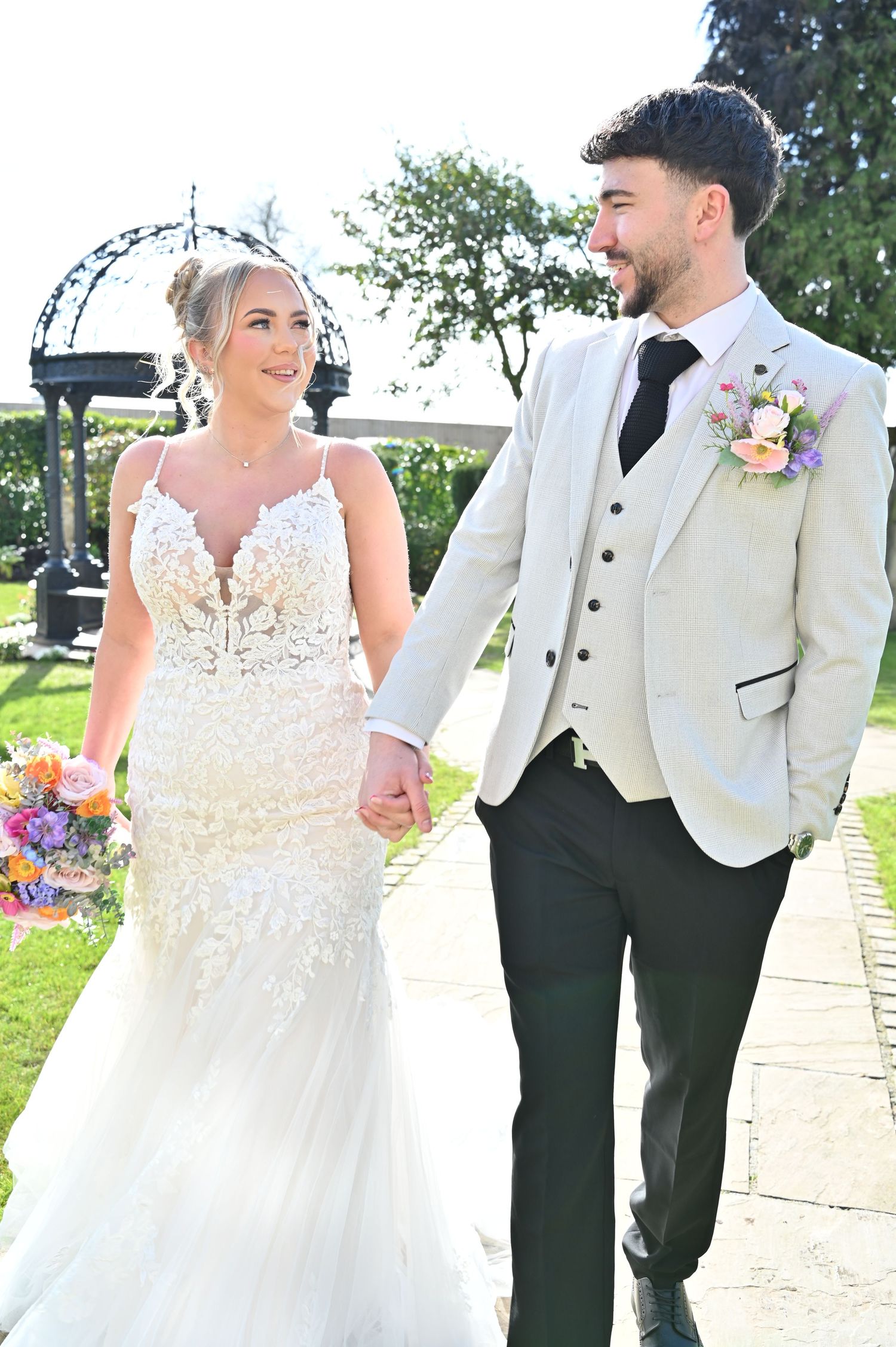 Bride and groom stand by tranquil pond near traditional tea house in garden setting.