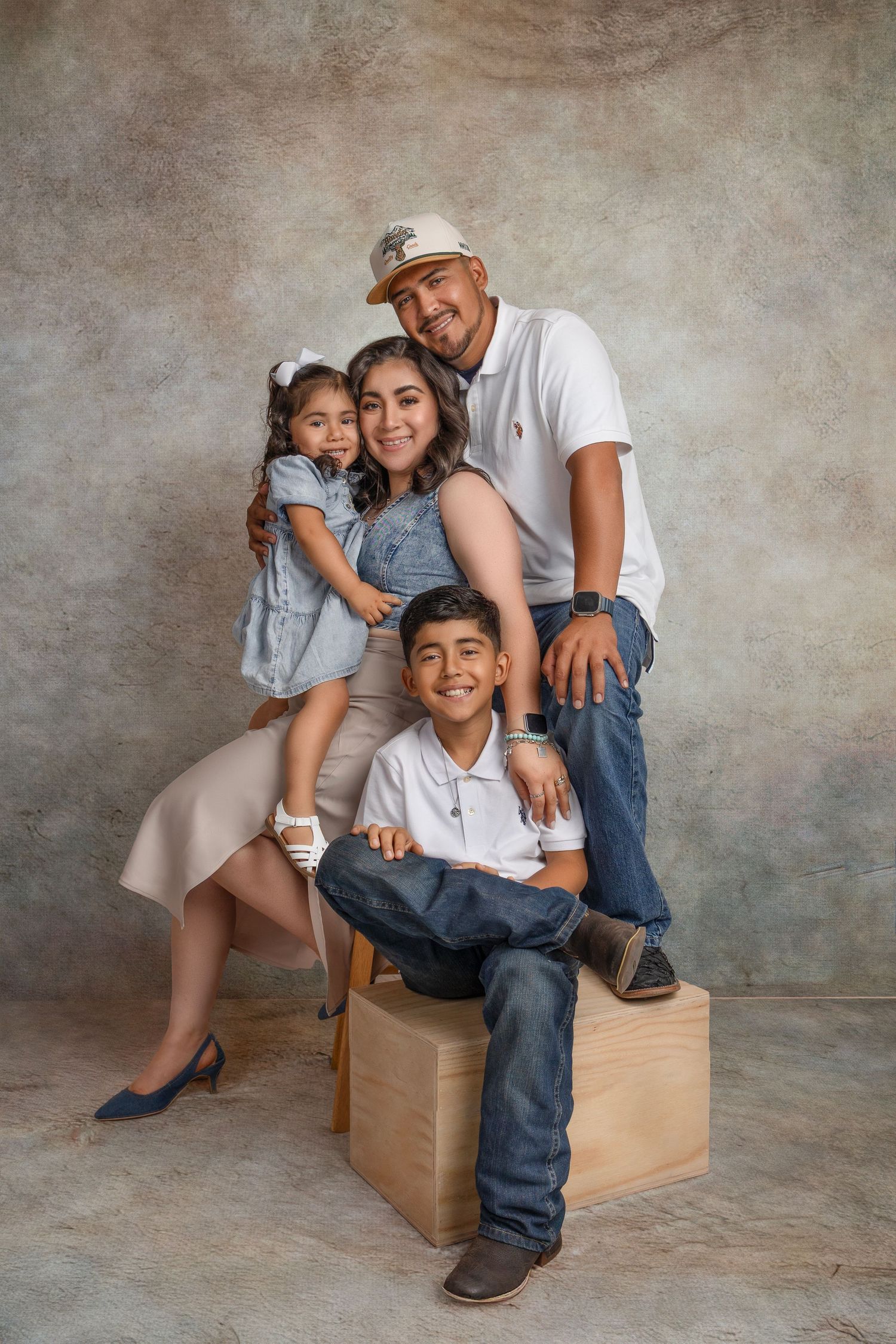 Professional studio portrait series of family sitting and posing together on wooden boxes against textured gray backdrop.
