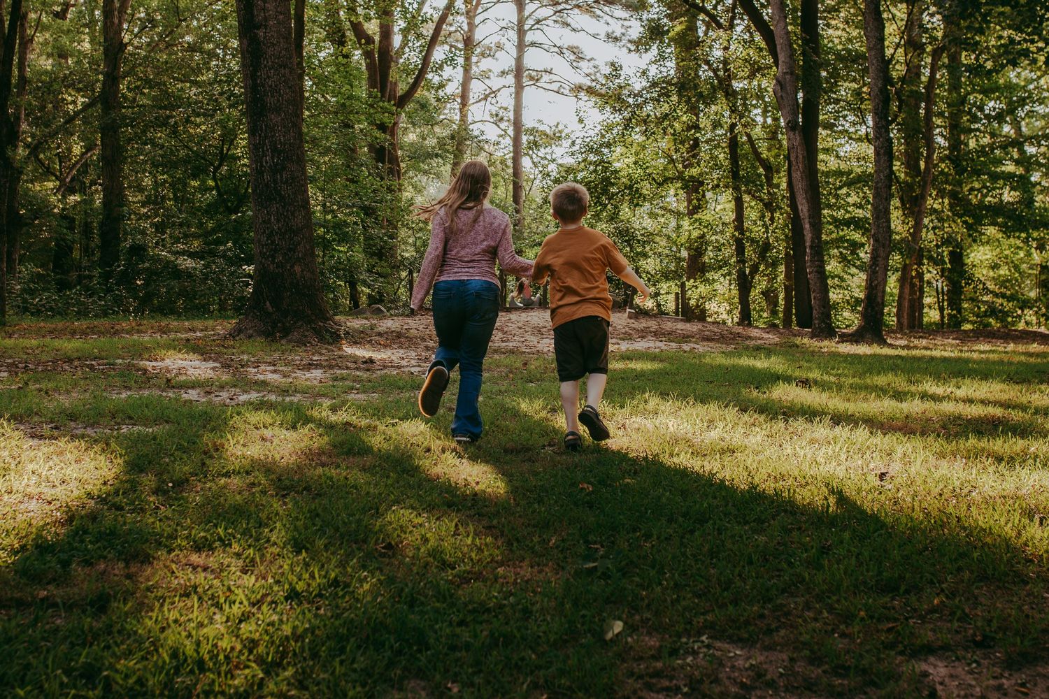 Mother and son holding hands while running through a lush green forest clearing on a sunny day. Whitney Popp, Phoenix Arizona photographer