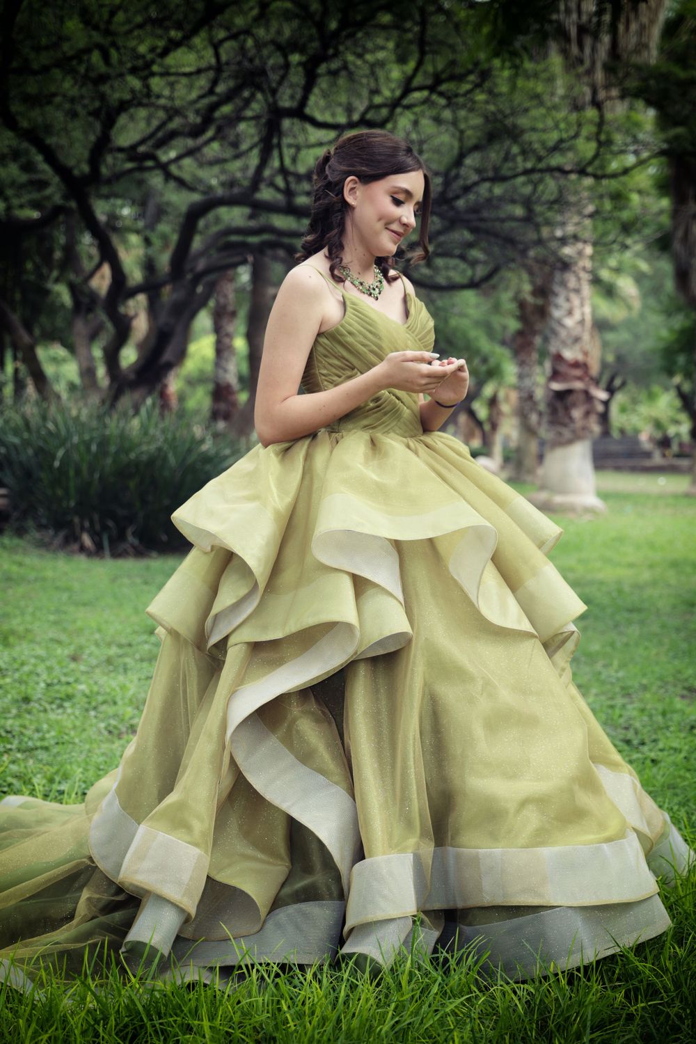 A person in a chartreuse ballgown checks their phone in a lush garden setting.