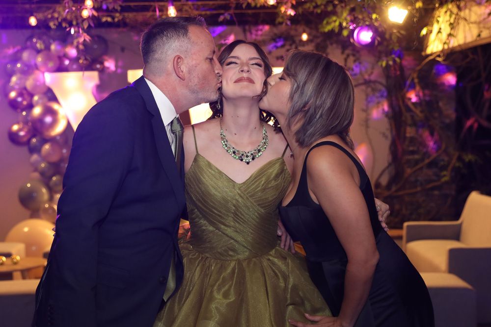 Three people share an affectionate moment at a celebration with purple lighting and bokeh effects.