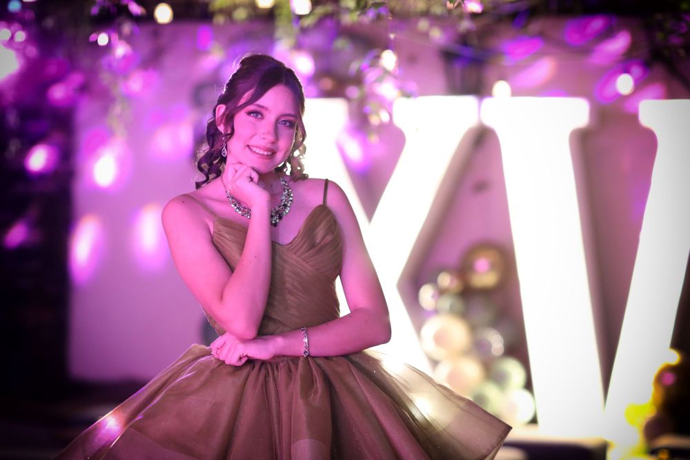 A person in an elegant olive gown poses near illuminated letter decor with purple ambient lighting.