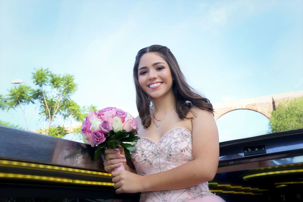 A celebrant in a pink dress holding a bouquet poses against a bright blue sky.