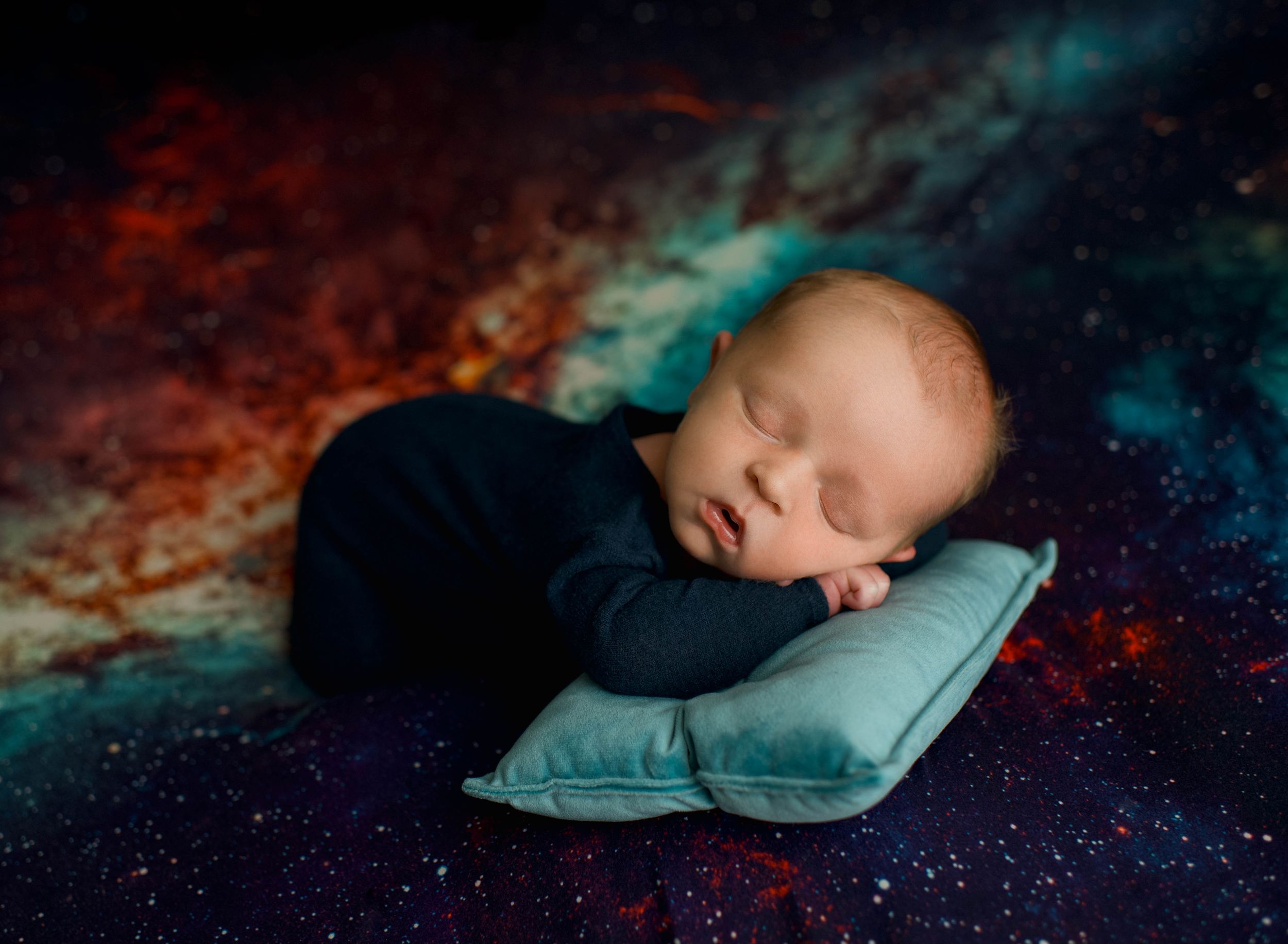 Artistic newborn photography with dark background and turquoise accents.