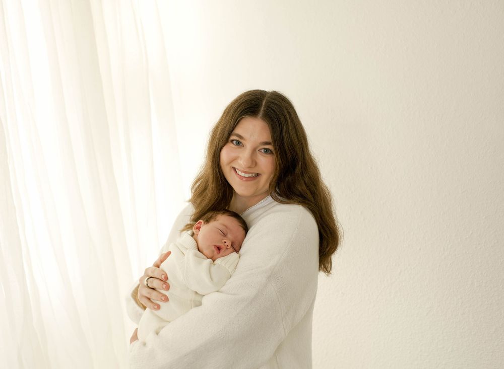A tender moment captured in soft light as a mother in white cradles her sleeping newborn baby.