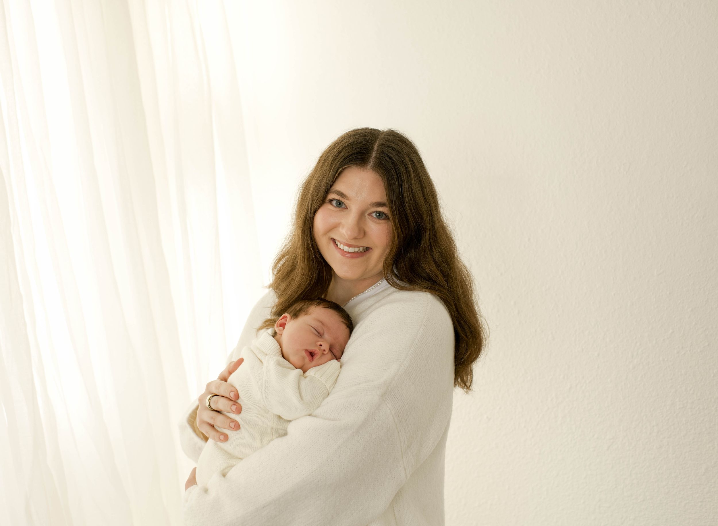 A tender moment captured in soft light as a mother in white cradles her sleeping newborn baby.