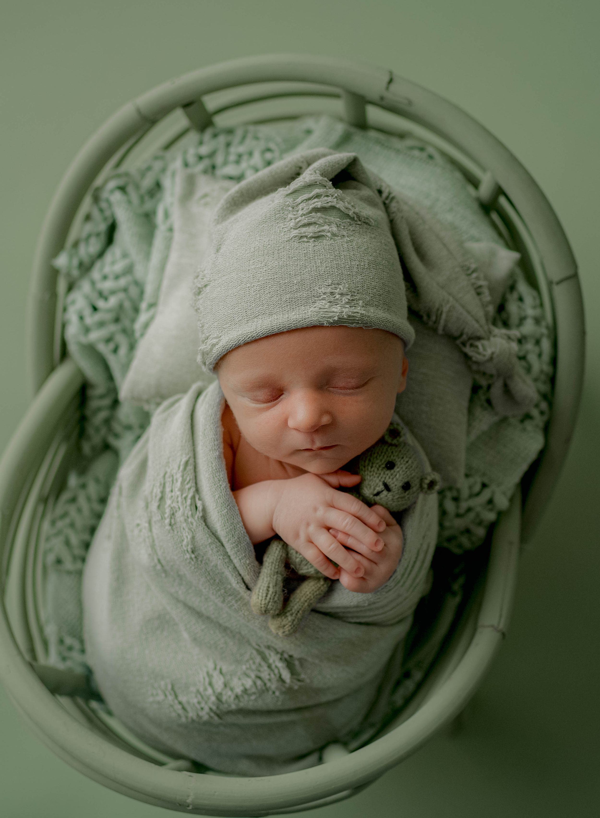 Overhead view of swaddled newborn in soft green tones.