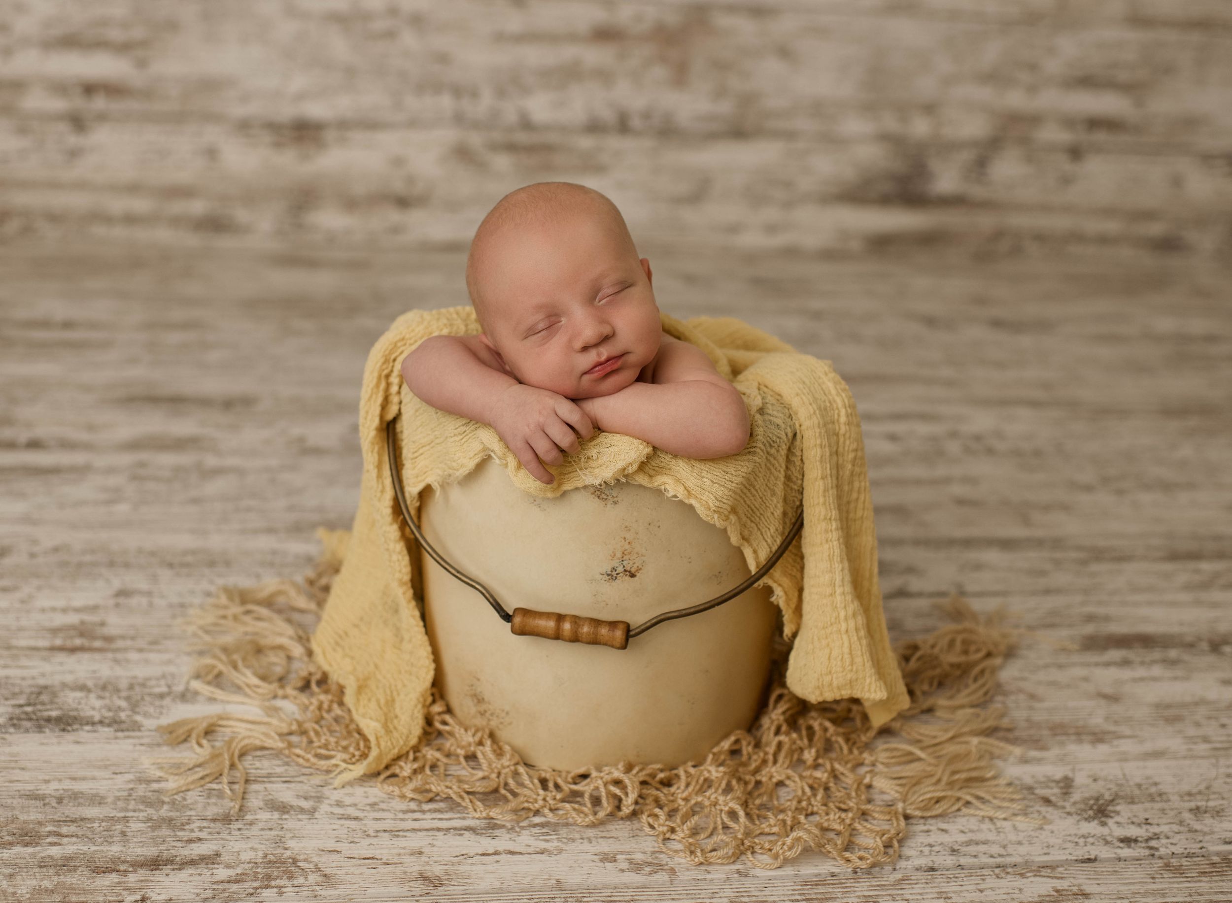 Three sequential photos of a sleeping newborn baby wrapped in soft yellow fabric nestled in a rustic wooden setting.