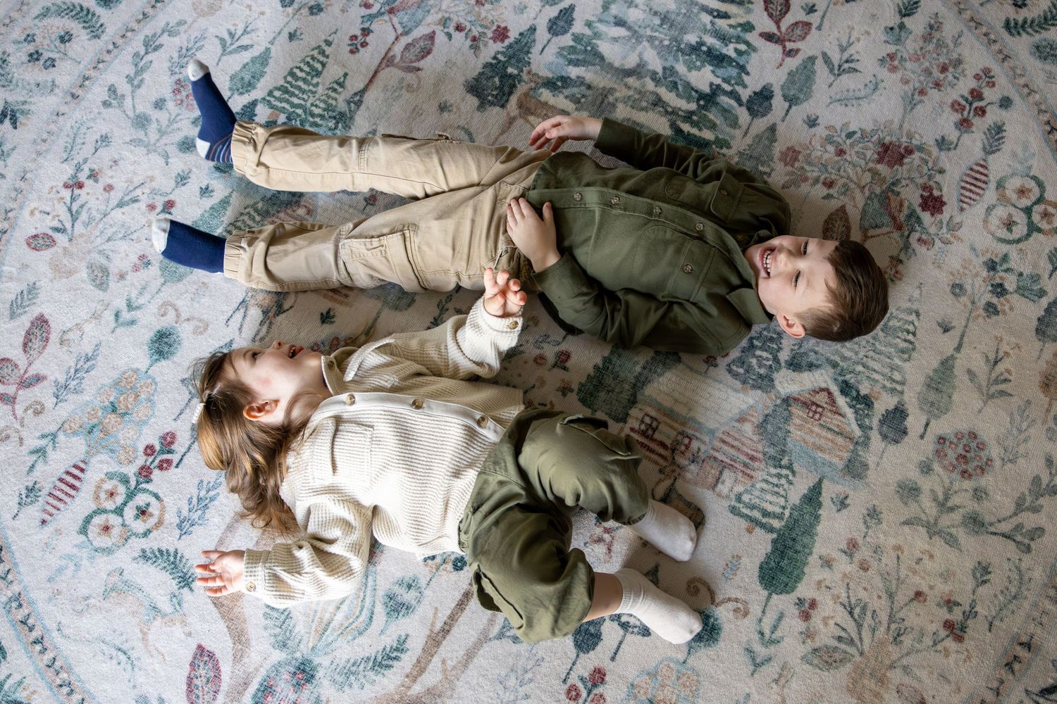 Three young children playing together on floral patterned rug viewed from above.