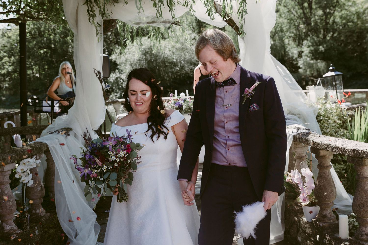 A couple shares a joyful moment under a white gazebo decorated with flowers.