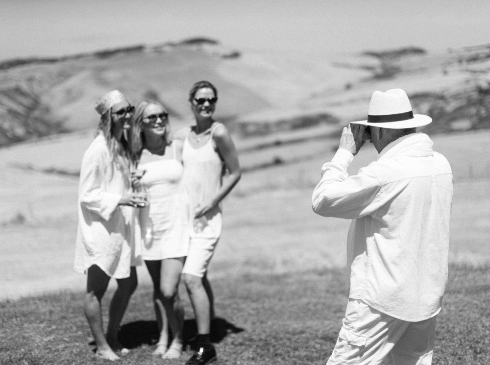 A man photographing three women in white dresses at a wedding pool party in Tuscany, Italy.