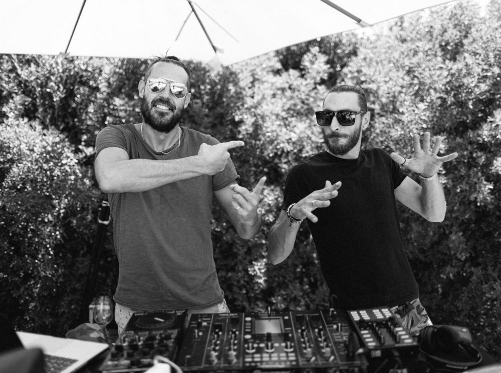 Two DJs by the table with an umbrella at a wedding pool party in Tuscany, Italy.