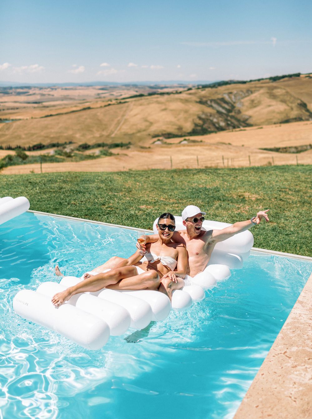 A bride and groom relaxing in a pool at a white wedding pool party in Tuscany, Italy.
