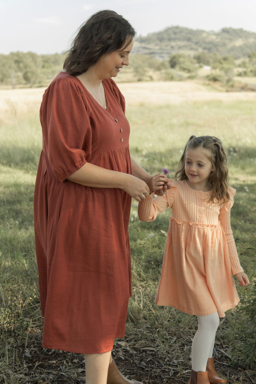 A parent and child share a playful moment while holding hands in a field.
