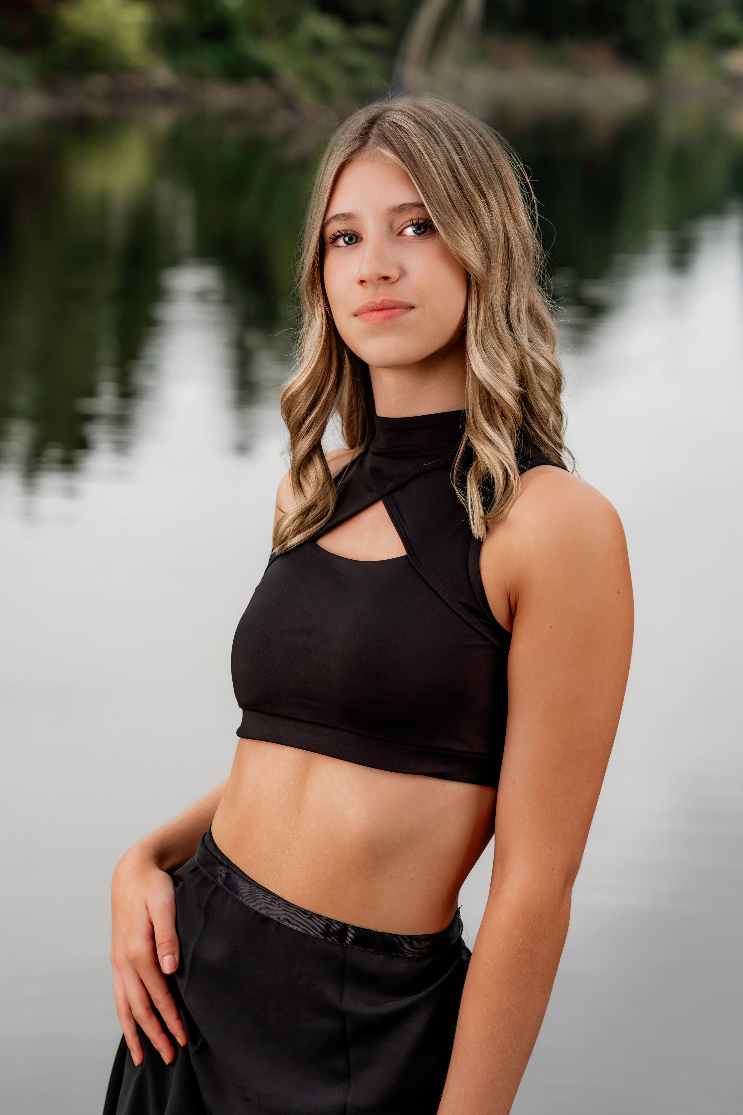 Lakeridge Highs School Dance Team Dancer in black athletic wear poses outdoors near a tranquil lake with soft natural lighting.