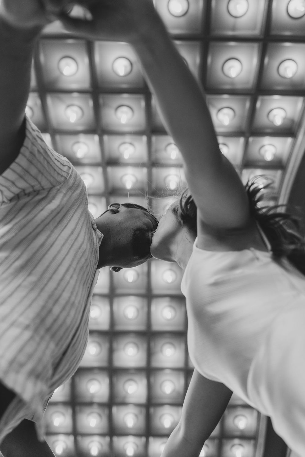 A black and white photo of a couple dancing under dramatic overhead lighting.