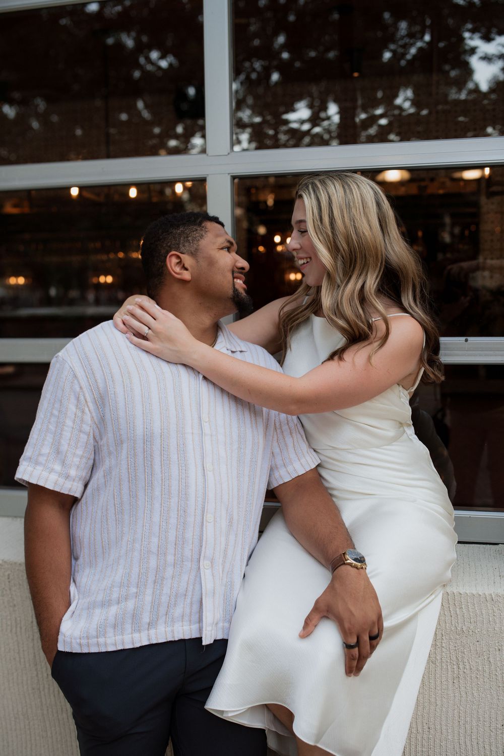 A couple in white and striped outfits share an intimate moment on a couch during a photoshoot.