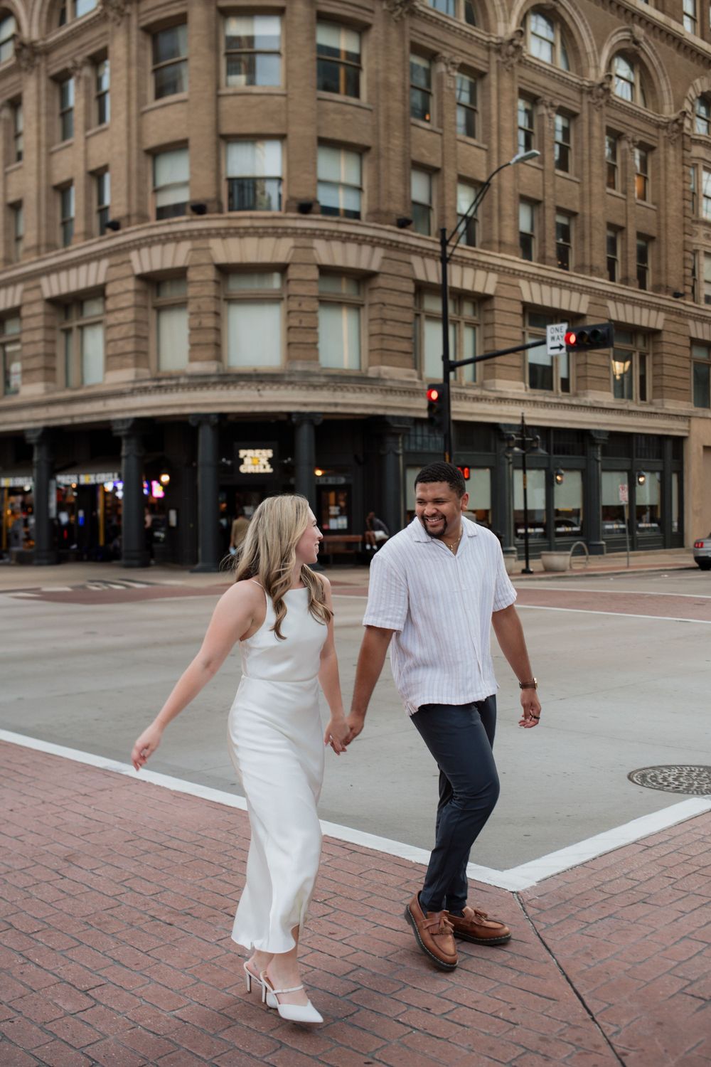A couple strolls hand in hand through an urban setting with historic brick buildings.